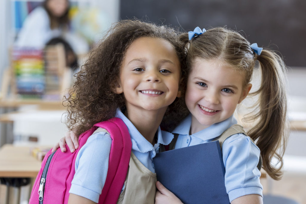 Adorable kindergarten or preschool students hug each other in their classroom.